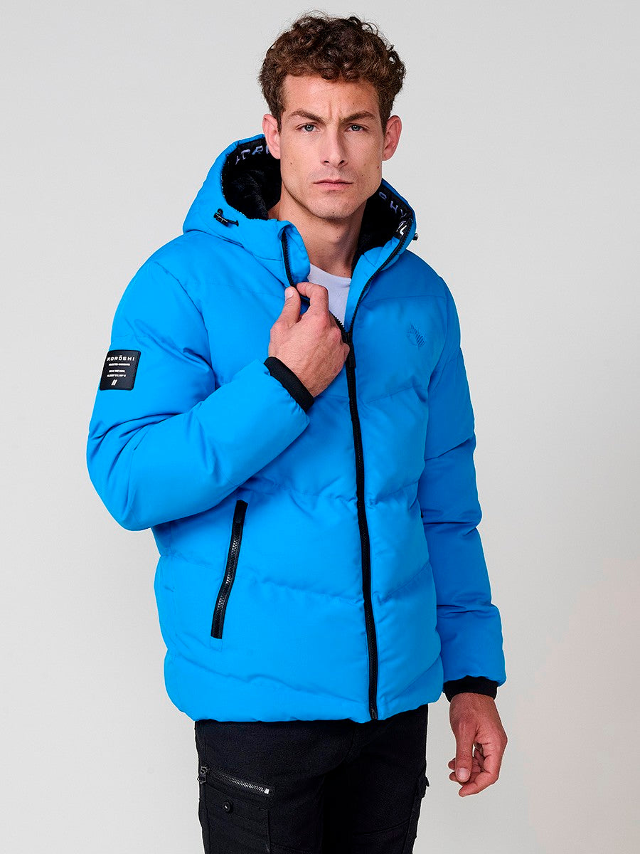 KORÖSHI. Cazadora acolchada azul claro de hombre con cuello alto, capucha, bolsillos y cierre delantero de cremallera.